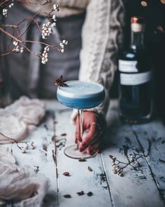 a person is holding a glass with some wine in it and flowers on the table