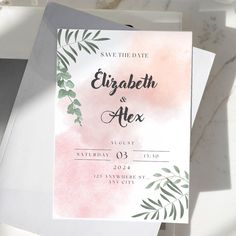 the wedding stationery is set on top of two envelopes with greenery and pink watercolor paint