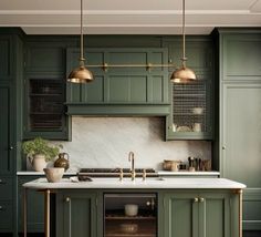 a kitchen with green cabinets and marble counter tops, gold pendant lights over the sink