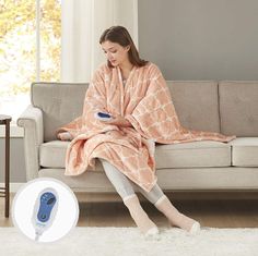 a woman sitting on a couch with a blanket over her and a hair dryer in front of her