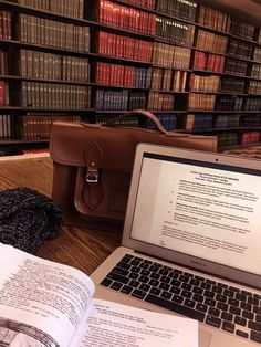 an open laptop computer sitting on top of a wooden table next to a book case