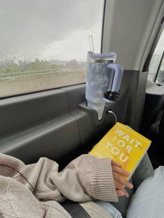 a person sitting in the back seat of a car holding a yellow book and looking out the window