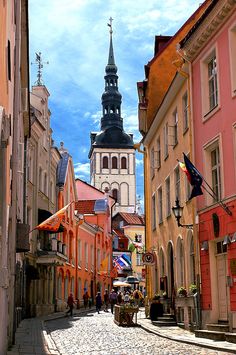 an old european city street with buildings and a church steeple in the back ground