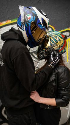 a man and woman wearing helmets standing in front of a graffiti covered wall with their backs to each other