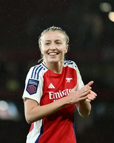 a female soccer player is smiling and holding her hands out in the air while wearing a red shirt