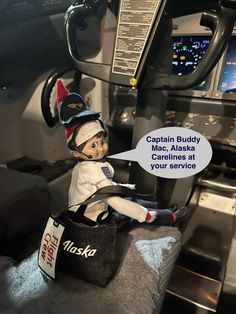 a small doll sitting on top of a bag in the cockpit of a plane with caption that says captain buddy mac alaska is your service