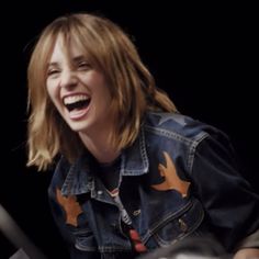 a woman laughing while sitting in front of a microphone and another person standing behind her