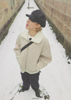 a young boy standing in the snow wearing a hat and jacket with his hands on his hips