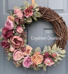 a wreath with pink flowers and greenery hanging on the front door to welcome guests