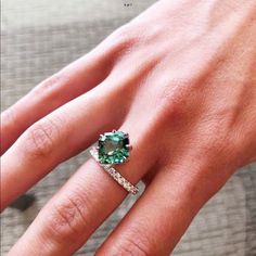 a woman's hand with a green ring on top of her finger and an emerald stone in the middle