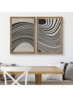 two black and white paintings hanging on the wall next to a wooden table with chairs