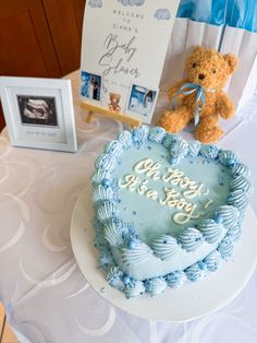 a teddy bear sitting next to a blue frosted heart shaped cake on a table