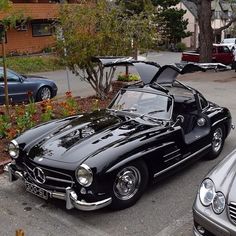 an old black mercedes sports car parked in a parking lot next to other classic cars