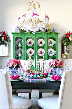 a dining room table decorated for christmas with green china cabinet and pink poinsettis