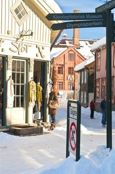 a woman standing in the snow next to a building and street sign with people walking by