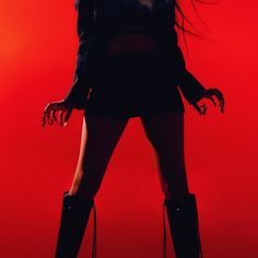 a woman with long hair and black boots posing in front of a red background,