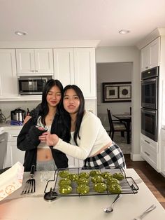 two women standing next to each other in a kitchen with food on the counter top