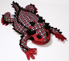 a red and black stuffed animal lizard on a white surface with its legs spread out