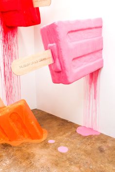 two popsicles are being sprayed with pink and orange paint in an art gallery setting