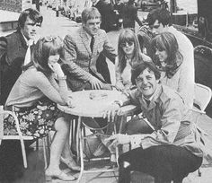 a group of people sitting around a table on top of a street side walk next to each other