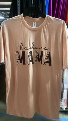 Stand out from the boring mom crowd with this Peach BADASS Mama Graphic T-shirt. Let your badassery shine while staying comfortable and looking stylish. This shirt is perfect for any mama who takes charge and doesn't take herself too seriously. FABRIC: cotton/poly blend  MEASUREMENTS:  Size Small - Bust:  Length:  Size 2XL - Bust:  Length:  CARE INSTRUCTIONS: DTG prints stay crisp and vibrant for a long time if you follow the care instructions. To keep them from fading or cracking, machine-wash garments on a gentle cycle, avoid bleach and fabric softeners, and don't iron the prints. LIVE FIT DESCRIPTION:  Be sure to watch the full FIT VID in the App (SHOP BAD HABIT) to see how it looks and fits on our Live Team!  SIZE GUIDE BHB BABES SIZING INFO:  The Owner, SARA (long blond hair), is wear Athletic Body Type, Long Blond, Live Girls, Live Fit, Bad Habit, Long Blonde Hair, High Rise Denim, Denim Flares, Colored Denim