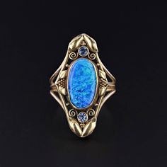 Antique Black Opal Ring: This ring features a vibrant, 3.42ct natural black opal with two natural sapphire accents.  The ring was created from an antique, 18k gold brooch (circa 1910) by removing the pin findings and adding a 14k gold band. The face of the ring measures 1.2 inches by 0.6 inches wide.  It is currently a size 7.25, but can be resized free of charge. The ring is in very good condition; however, there is a small crimp on the collet (bottom, left in the photo) suggestive of a past repair.  Upon purchase, your ring will arrive elegantly packaged, ready for gifting or as a special treat for yourself.  We carefully wrap each piece to ensure a delightful unboxing experience. We also offer free and flexible layaway plans, so take advantage of this option to make owning your dream pi Antique Opal Rings For Collectors, Antique Opal Rings Collectible, Antique Opal Rings For Collectible, Victorian Style Opal Ring For Formal Occasions, Antique Style Opal Ring For Formal Occasions, Antique Opal Ring For Formal Occasions, Victorian Opal Cabochon Ring For Collectors, Victorian Cabochon Opal Ring Collectible, Victorian Style Collectible Cabochon Opal Ring