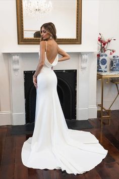 a woman standing in front of a fire place wearing a white dress with open back