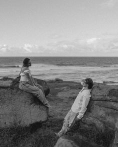 two people sitting on rocks near the ocean