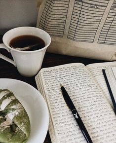 a cup of coffee next to an open book and some pastries on a table