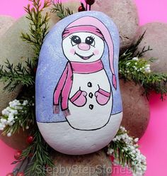 a painted rock with an image of a snowman on it, surrounded by rocks and flowers