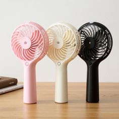 three different colored fans sitting on top of a wooden table