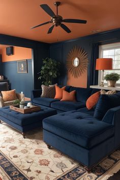 a living room with blue couches and orange accents on the walls, an area rug and a ceiling fan