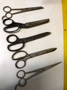 five pairs of scissors sitting on top of a white table next to each other with black handles