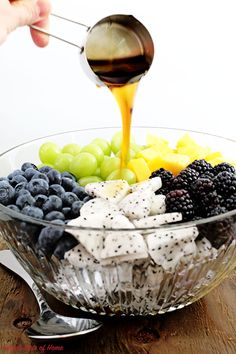 a person pouring dressing over a bowl of grapes, blueberries, and blackberries