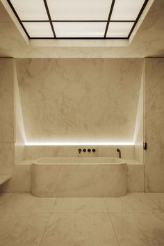 an empty bathroom with white marble walls and floor, along with a skylight above the bathtub