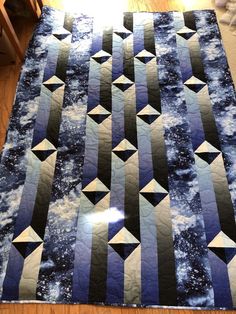 a blue and white quilt on the floor with stars in the night sky behind it