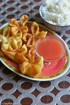 a plate with wontons on it next to a bowl of rice and sauce