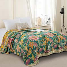 a bed covered in a green and yellow floral comforter next to a white window