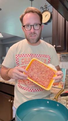 a man in glasses holding up a large square pan filled with food on top of a kitchen counter