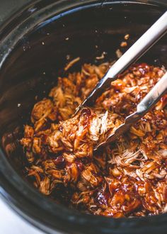 two tongs in a slow cooker filled with shredded meat and bbq sauce