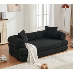 a black couch sitting on top of a hard wood floor next to a white rug