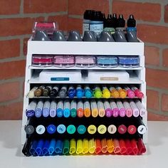 a white shelf filled with lots of different colored crayons and paint bottles next to a brick wall