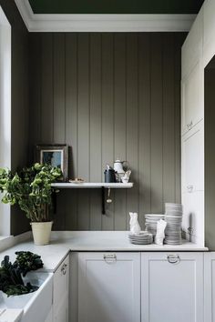 a kitchen with green painted walls and white cupboards, potted plants on the window sill