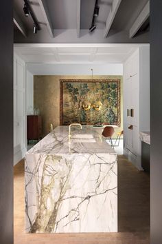 a large marble counter top in a room with white walls and wood flooring, along with a painting on the wall