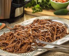 a plate full of shredded beef on a table with a crock pot in the background