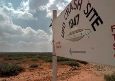 a sign in the middle of nowhere with clouds in the sky behind it and an arrow pointing up