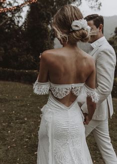 a bride and groom standing in the grass with their back to the camera, looking at each other