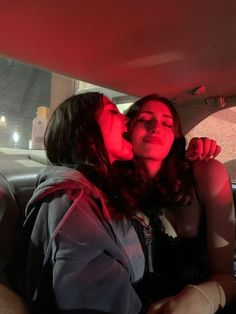 two women sitting in the back seat of a car, one is kissing the other