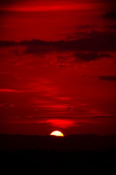 the sun is setting behind some clouds in the sky with red and yellow hues