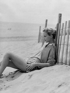 a woman sitting on the beach next to a fence